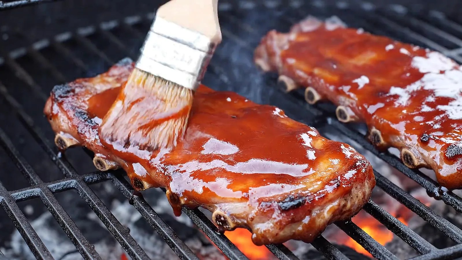 Barbecue sauce being brushed over ribs on the grill